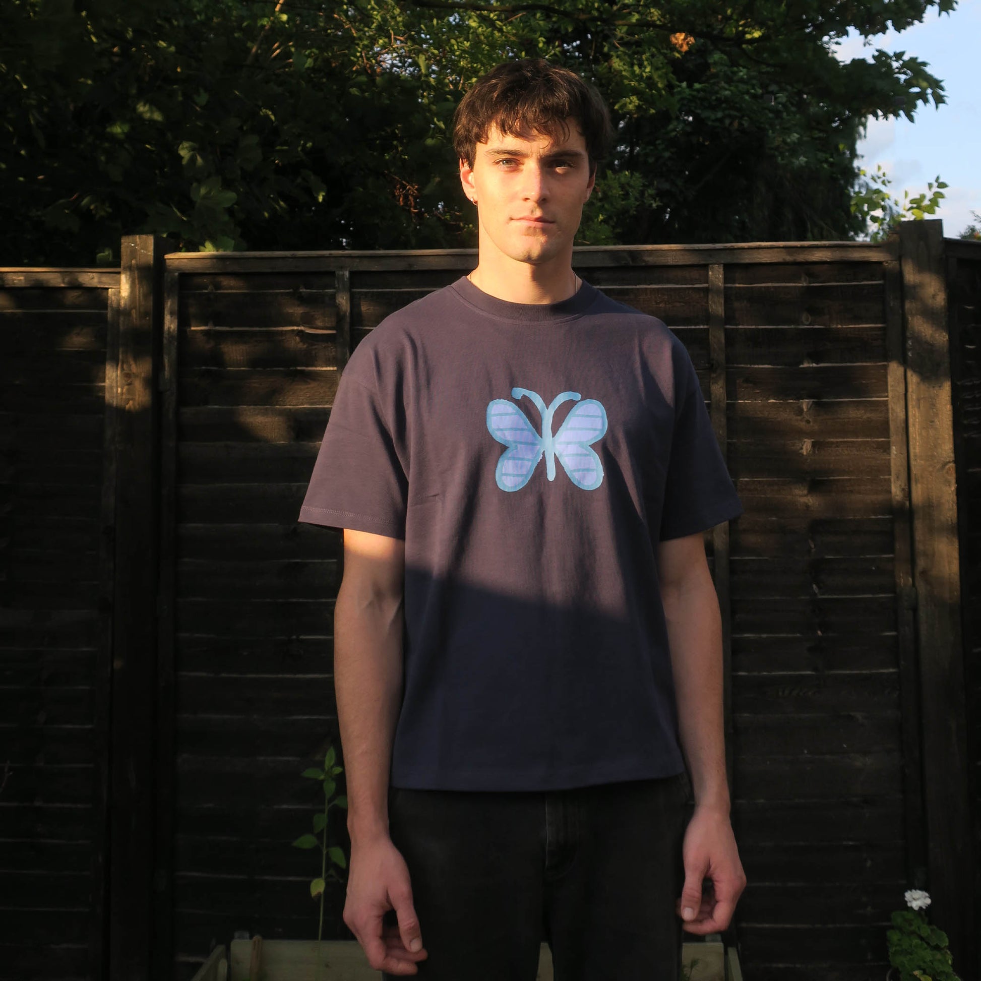 Person wearing a navy t-shirt with a blue butterfly design outdoors.
