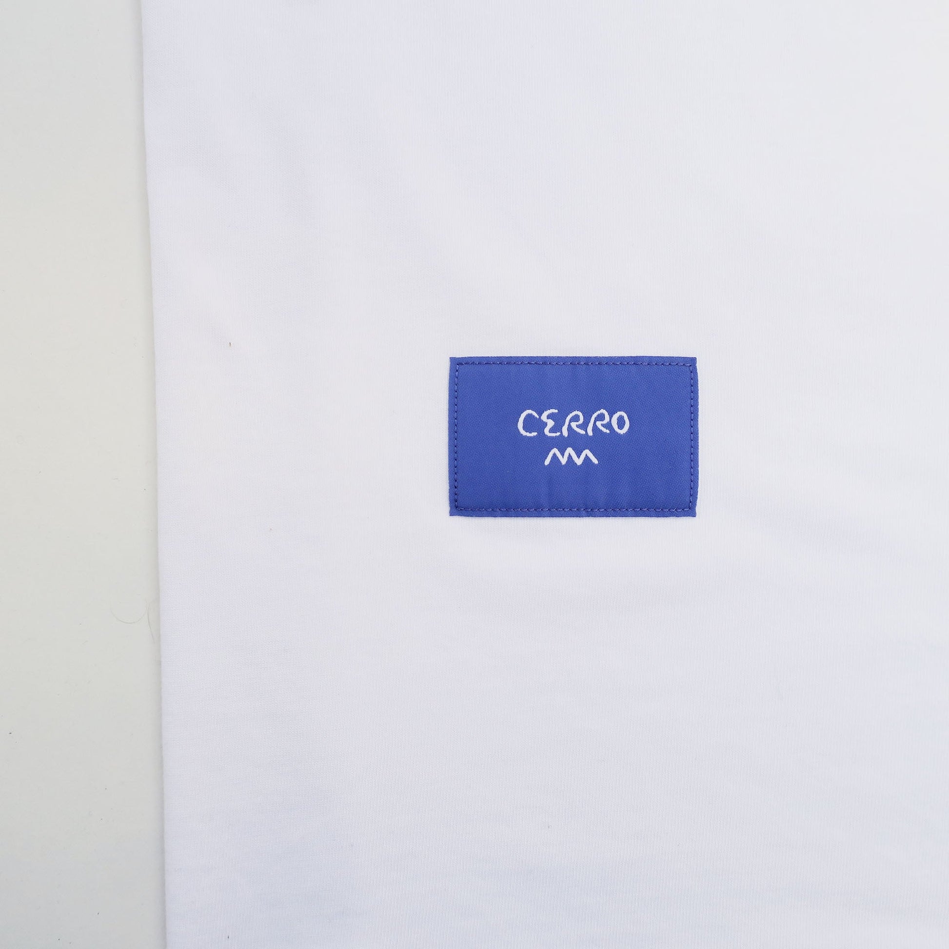 White shirt with a blue label featuring the brand 'Cerro' on a light gray background