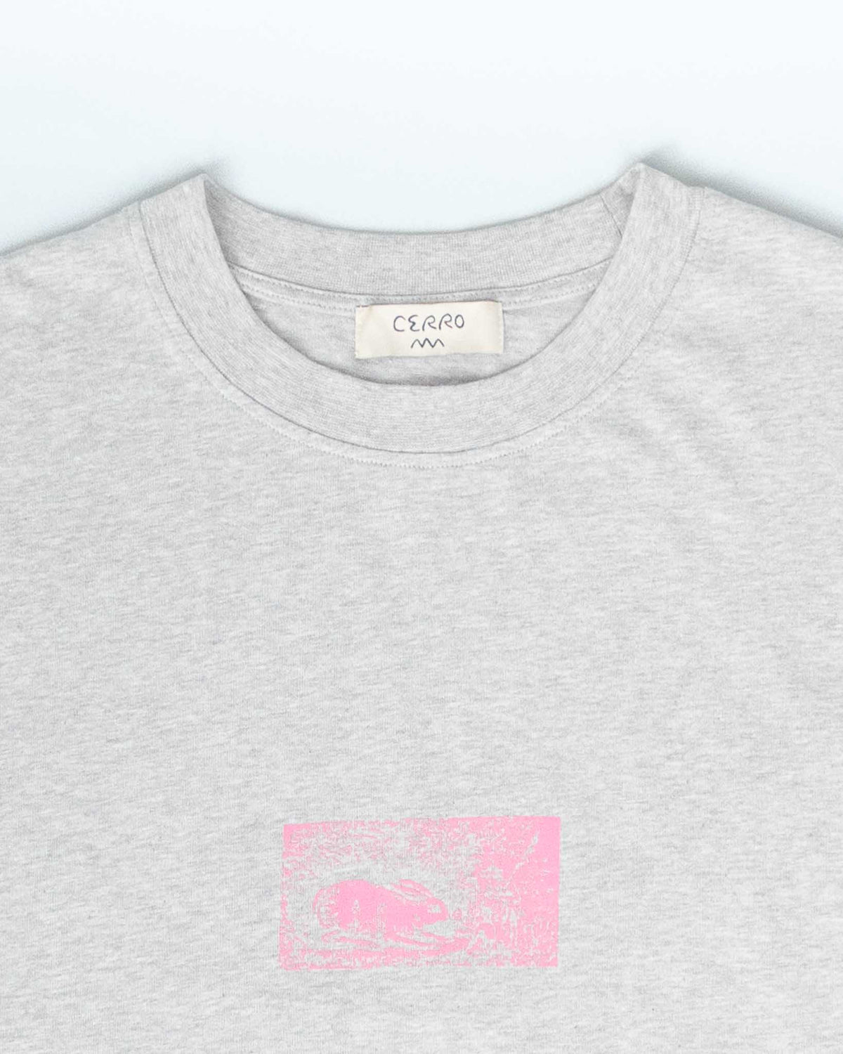 Close-up of a light heather gray crewneck t-shirt by CERRO, featuring a small pink graphic print on the chest.