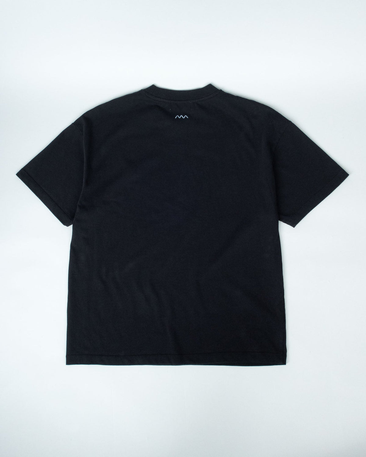 A black short-sleeve crewneck t-shirt laid flat against a light gray background, showing a small white logo on the inside back neckline.