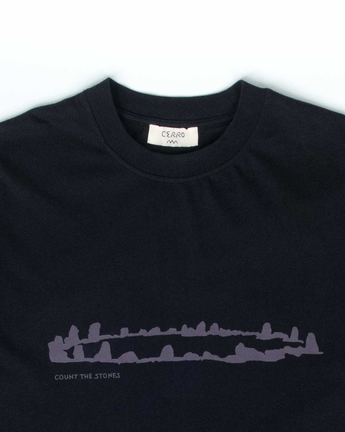 A close-up of a black crewneck t-shirt by Ciarro, featuring a light purple line-art graphic of a stone circle with the text 'COUNT THE STONES' printed below it.